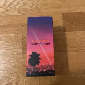 City of Stars Eau de Parfum från Louis Vuitton - City of Stars Eau de Parfum från Louis Vuitton kommer i en elegant glasflaska med en svart kork. Förpackningen har en vacker gradient i lila och rosa med en palmmotiv. Parfymen utstrålar en känsla av lyx och exklusivitet.