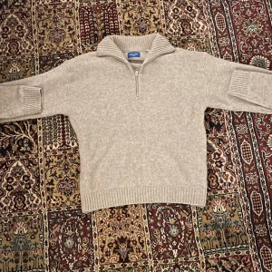 Beige stickad tröja från Jack and Jones  - Säljer en stilren beige stickad tröja från Jack and Jones. Tröjan har en praktisk dragkedja vid halsen och ribbade detaljer vid ärmslut och nederkant. Perfekt för kyligare dagar. Nypris var 600kr.