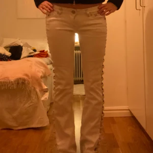 Beige bootcut byxor med snörning - Snygga beige bootcut byxor med unik snörning längs sidorna. Perfekta för en trendig look. Byxorna har en lågmidjad passform och knappar framtill.