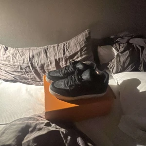 Svarta sneakers från Louis Vuitton - Stilrena svarta sneakers från Louis Vuitton med monogrammönster. Skorna har en vit sula och snörning framtill. Perfekta för en trendig look. Det ingår box också passar 42-45