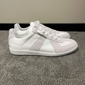 Maison margiela skor - Snygga vita sneakers med grå mockadetaljer och snörning. Perfekta för en stilren look. Skorna har en klassisk design med en bekväm sula och är ifrån märket Maison margiela. Självklart äkta, kvitto finns. Skriv för mer!!