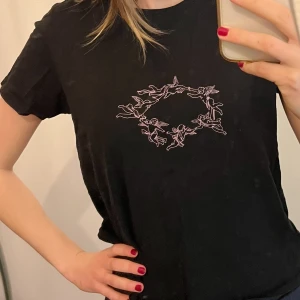 Svart t-shirt med änglamotiv - Svart t-shirt med ett unikt änglamotiv i ljusmila på framsidan. Använd ett par gånger men är i bra skick. Lappen med storlek är borttagen men skulle säga att den är S eller M