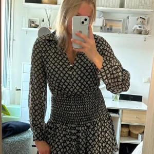 Svart och vit mönstrad klänning - Snygg svart och vit mönstrad klänning med långa ärmar och knappar framtill. Helt slutsåld! Och kostar typ 399 nypris, kan posta direkt!!!