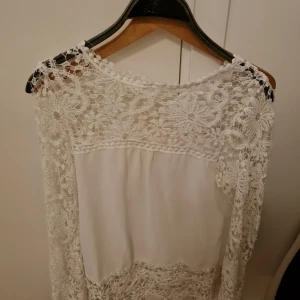 Vit spetsblus - Elegant vit blus med vackra spetsdetaljer och blommönster. Perfekt för en stilren look med långärmad design och en luftig passform.