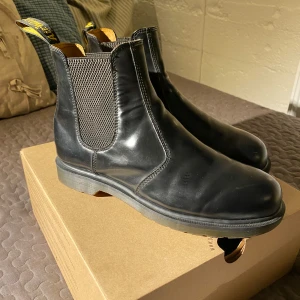 Svarta Chelsea boots från Dr. Martens - Säljer ett par klassiska svarta Chelsea boots från Dr. Martens. Skorna är tillverkade i slätt skinn och har elastiska paneler på sidorna för enkel på- och avtagning. Perfekta för både stil och komfort. Kvitto och box finns. Säljer dom då de inte används längre. Hör gärna av dig vid frågor  