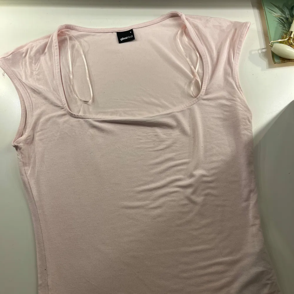 Säljer en ljusrosa topp från Gina Tricot med fyrkantig halsringning. Toppen är ärmlös och i ett mjukt material, soft touch. Jättefint skick då den knappt är använd. Den ser urtvättad ut på bilden men den är fortfarande i fin färg!!!. Yläosat.