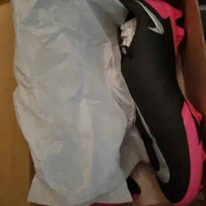 Nike Phantom fotbollsskor - Snygga Nike Phantom fotbollsskor i svart och rosa med vita detaljer. Skorna har snörning och en slitstark sula med dobbar för optimalt grepp på planen. Perfekta för fotbollsspelare som vill ha både stil och funktion. Helt nya säljer för att jag beställde fel storlek 