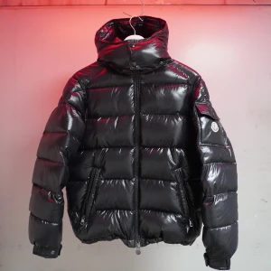 Svart pufferjacka från Moncler - Säljer en snygg svart pufferjacka från Moncler. Jackan har en glansig finish och är utrustad med en dragkedja framtill. Den har en huva och långa ärmar, samt Monclers logotyp på ärmen. Perfekt för kyliga dagar!