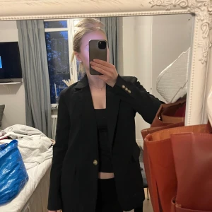 Svart blazer - Snygg svart kavaj från ginatricot med klassisk design och knappar framtill. Perfekt för en stilren look. Passar bra till både byxor och kjol. Sparsamt använd. Säljer då den tyvärr inte kommer till användning 