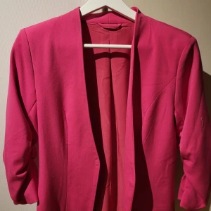 Rosa kavaj från Vila - Snygg rosa kavaj från Vila i en härlig färg. Perfekt för att liva upp garderoben. Kavajen har en öppen design utan knappar och trekvartsärmar som ger en modern look.