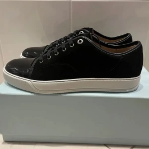Lanvin Sneakers - Stilrena svarta sneakers från Lanvin med en blank tå och vita sulor. Skorna har snörning och är tillverkade i en kombination av skinn och syntetmaterial. Perfekta för en elegant och modern look, jätte snygga skor från lanvins, storlek 41