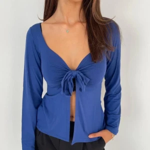 Design by si blus - Snygg blå långärmad topp med knyt framtill. Toppen har en djup v-ringning och är perfekt för en stilren look. Materialet ser mjukt och bekvämt ut.