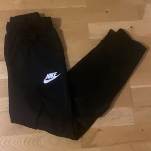 Svarta Nike byxor  - Säljer ett par svarta mjukisbyxor från Nike med elastisk midja och det klassiska Nike-loggan i vitt på benet. Perfekta för en avslappnad stil eller träning.