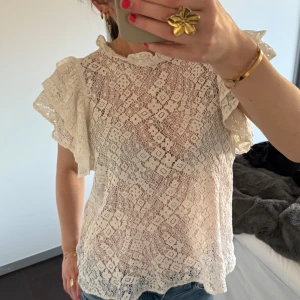 Vit spetsblus - Säljer en söt vit spetsblus med korta ärmar och volangdetaljer. Perfekt för en romantisk look. Blusen har ett vackert mönster och är lätt och luftig.