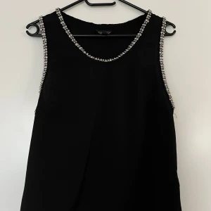 Topp, Topshop, 40, svart - Svart topp med fina silvriga strassdetaljer från Top Shop i storlek M. I mycket fint skick. 100% viskos.   Mått: Längd ca 55 cm Byst ca 50 cm Midja ca 50 cm