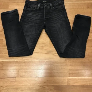 Svarta jeansbyxor från jack n Jones  - Snygga svarta jeansbyxor från Jack n Jones med en klassisk femficksdesign. Byxorna har en knappgylf och är tillverkade i ett slitstarkt denimtyg. Perfekta för en stilren look.