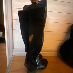 Svarta höga stövlar med dragkedja - Snygga svarta stövlar i skinn med hög skaft och dragkedja längs sidan. Stilrena och enkla att matcha med olika outfits. Om man kollar nära ser man lite defekt på tårna. 