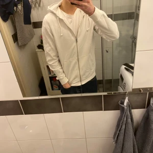 Hoodie med dragkedja  - Säljer en stilren vit hoodie med dragkedja och huva. Den har långa ärmar och en bekväm passform. Perfekt för en avslappnad look. Hör av dig vid intresse! Storlek M