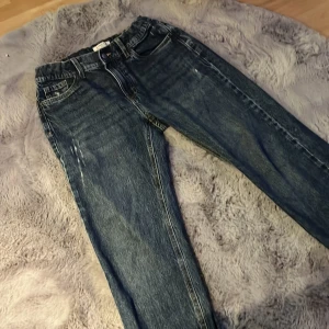 Blå jeans från Lindex - Snygga blå jeans från Lindex med klassisk femficksdesign och knappgylf. De har en avslappnad passform och är perfekta för en casual look. Jeansen har en lätt tvättad effekt som ger dem en cool vintagekänsla.