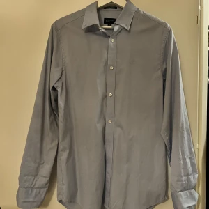 Grå/blå skjorta från GANT - Snygg grå/blå skjorta från GANT i storlek S. Klassisk design med knappar hela vägen och långärmad stil. 