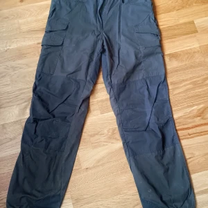 Mörkgröna vandring byxor med fickor - Säljer ett par mörkgröna vandring/friluftsbyxor med flera praktiska fickor på sidorna. Byxorna har en loose passform och är perfekta för en avslappnad stil. De är tillverkade i ett slitstarkt material som passar bra för utomhusaktiviteter. Vandring byxa från märke T&P workwear i storlek C52 (motsvarar L herr storlek)  Använt några gånger, som ny.