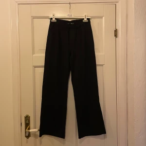 ostymbyxor  - Svarta byxor i skönt stretchigt material, hög midja och vida ben. Perfekta för en stilren look. Två fickor fram och två fejk bak. Använda en gång 