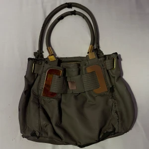 Grå grön hand väska  - Vintage grå grön handväska med guld detaljer. En ficka där bak och fyra innuti, två av dom med dragskedja alla skedjor fungerar. Materialet håller på att ramla av. 