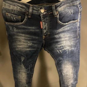 Blå jeans från Dsquared2 - Säljer ett par snygga blå jeans från Dsquared2 i storlek 42. De har en cool slitningseffekt och klassisk femficksdesign. Perfekta för en avslappnad men stilren look. Passar både till vardags och fest!