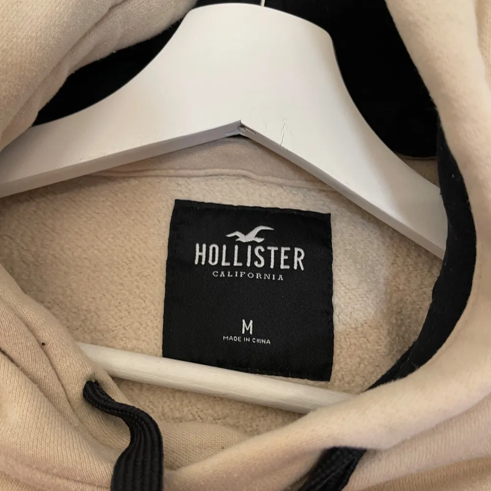 Säljer en snygg beige hoodie från Hollister i storlek M. Den har en klassisk design med en känguruficka och svarta dragsnören vid huvan. Perfekt för en avslappnad stil under höst och vår. Supermjuk och bekväm!. Tröjor & Koftor.