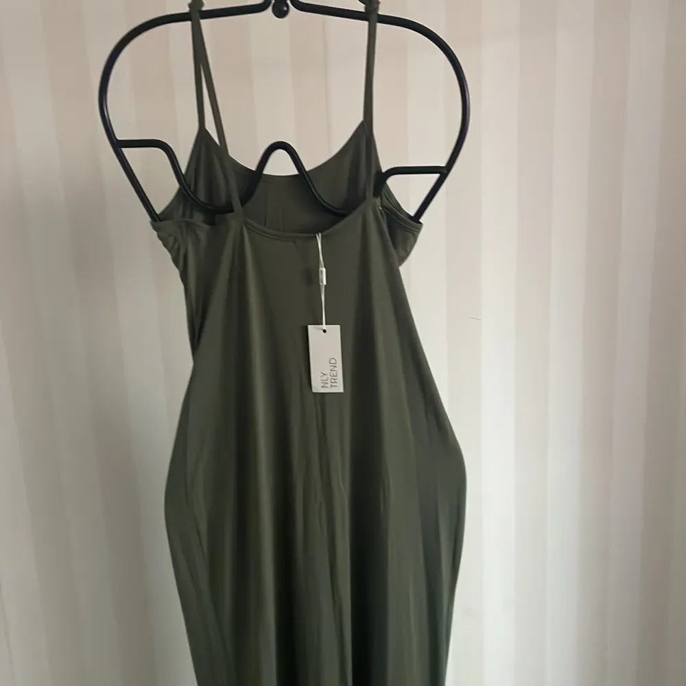 Snygg olivgrön långklänning från Nelly med smala axelband. Perfekt för sommardagar eller en avslappnad kväll. Klänningen har en enkel och stilren design som gör den lätt att matcha med olika accessoarer.. Mekot.