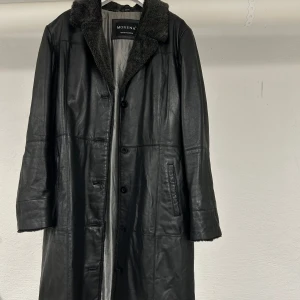 Skinnkappa - Svart Medellång skinnkappa i äkta läder med fusk päls på kragen i grått🖤 Väldigt fint skick ✨ Passar från strl 38-40 skulle jag säga beroende på hur du vill att den ska sitta 