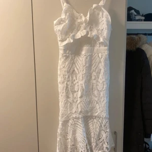 Vit spetsklänning med volangdetaljer - Säljer en superfin vit klänning i spets med volangdetaljer. Den har en figurnära passform och är perfekt för sommarens fester. Klänningen är axelbandslös och har en vacker spetsdesign som ger en romantisk känsla. Perfekt för student eller midsommar!