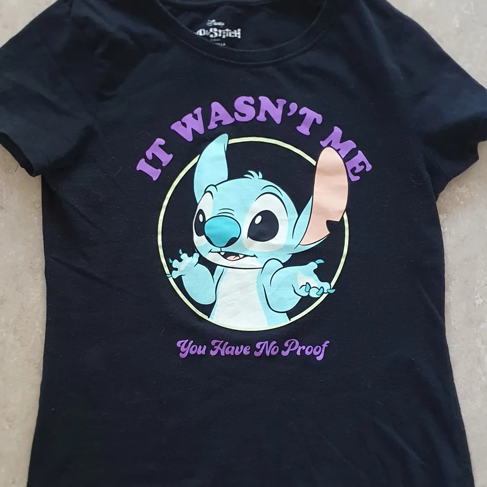 Säljer en svart t-shirt med ett coolt tryck av Stitch från Disney. Texten 'It Wasn't Me, You Have No Proof' står i lila ovanför och under bilden. Perfekt för alla Disney-fans som vill ha en rolig och avslappnad stil. T-shirten är kortärmad och gjord i mjukt bomullsmaterial.. T-shirts.