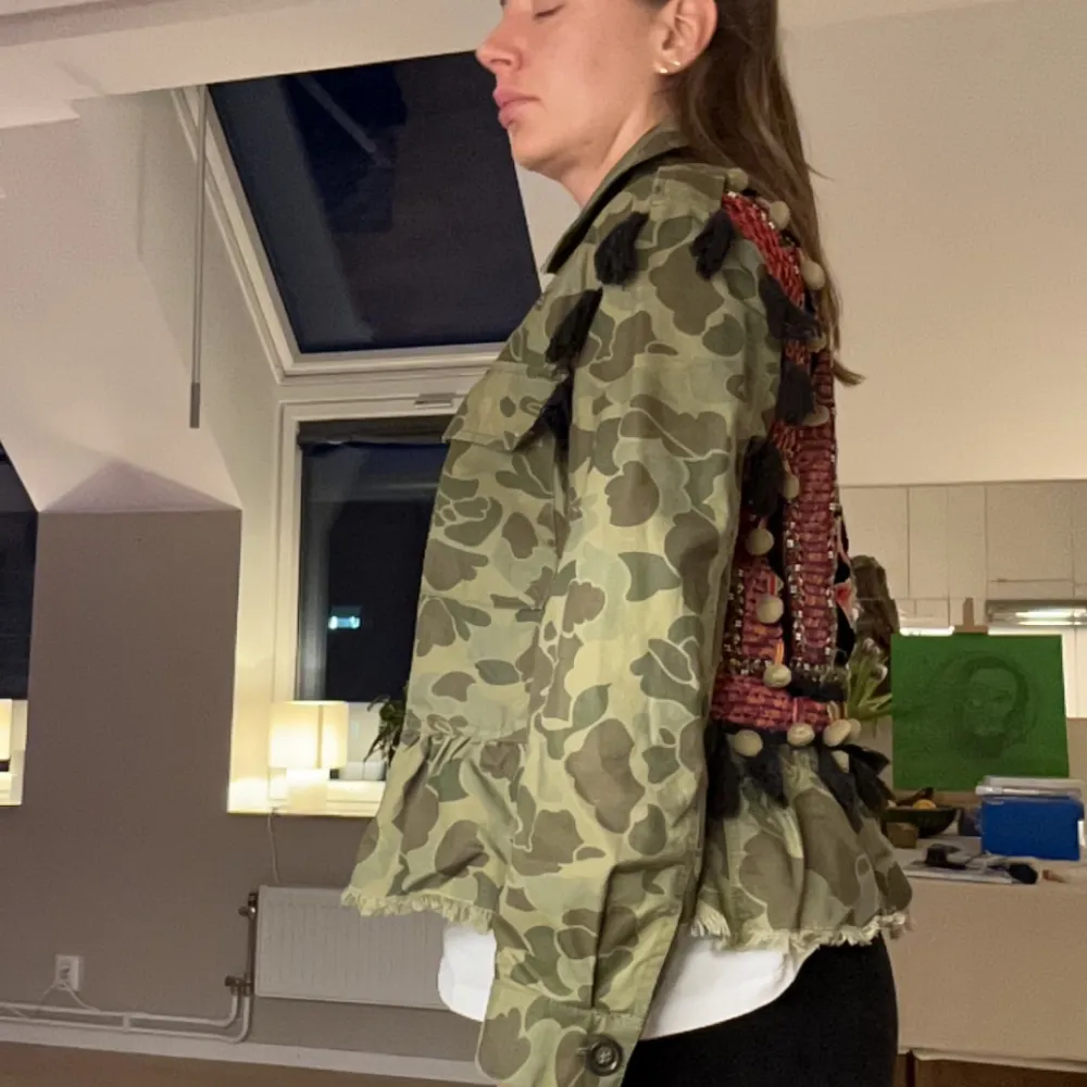 Säljer en unik camouflagejacka med coola broderier och tofsar på ryggen. Jackan har en loose passform och är perfekt för höst och vår. Den har knappar framtill och långa ärmar. Perfekt för dig som vill sticka ut!. Jackor.