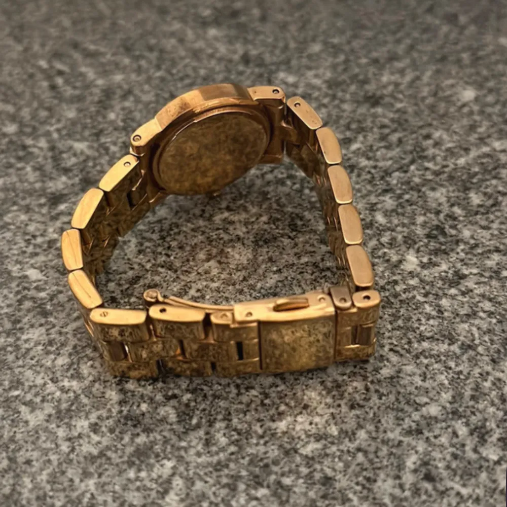 Snygg guldfärgad klocka från Marc Jacobs med vit urtavla och glittriga stenar som timmarkeringar. Armbandet är i metall och har en klassisk design. Perfekt för både vardag och fest! Diameter: 26,00 mm Tjocklek: 8,00mm Guld länk med vita kristaller . Asusteet.