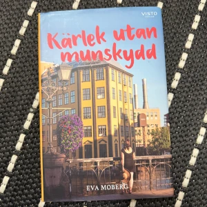 Kärlek utan munskydd - Boken 'Kärlek utan munskydd' av Eva Moberg är en roman som utspelar sig under pandemin. Den handlar om tre singlar och deras liv under tre månader i Norrköping. Omslaget visar en solig stadsmiljö med en kvinna som går över en bro. Perfekt för dig som gillar samtida berättelser med en twist av romantik och humor!