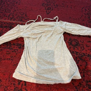 Grå offshoulder topp - Säljer en snygg grå offshoulder topp med långa ärmar. Perfekt för både vardag och fest! Den är i ett mjukt och bekvämt material som känns skönt mot huden. Passar bra till jeans eller kjol för en stilren look.