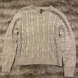 Grå stickad tröja från H&M - Säljer en mysig grå stickad tröja från H&M. Perfekt för kyliga dagar med sitt klassiska mönster och bekväma passform. Tröjan har långa ärmar och ribbade kanter vid ärmslut och nederkant. Passar både till vardags och lite finare tillfällen.