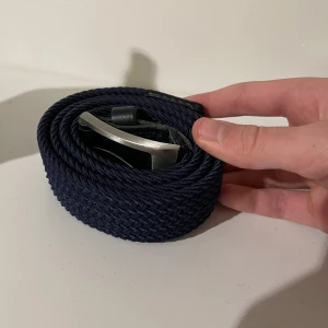 Mörkblått flätat bälte - Säljer ett snyggt mörkblått flätat bälte med en stilren silverfärgad spänne. Perfekt för både vardag och fest! Bältet är i mycket bra skick och passar till många olika outfits. Ett måste i garderoben för den som gillar att mixa stil och funktion.