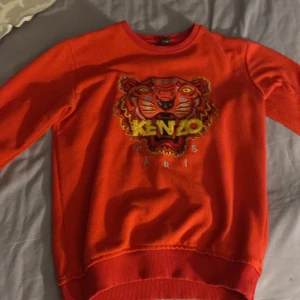 Röd tröja från Kenzo med tigerbroderi - Säljer en cool röd tröja från Kenzo med ett stort tigerbroderi på framsidan. Tröjan har långa ärmar och är i bra skick, perfekt för höst och vår. Den är gjord i ett mjukt material som känns skönt mot huden. Passar både till vardags och festliga tillfällen. 🐯