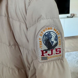 Beige dunjacka från Parajumpers - Säljer en superlätt beige dunjacka från Parajumpers i storlek S. Jackan har en snygg patch på ärmen och dragkedja framtill. Perfekt för höst och vår, håller dig varm utan att bli för tung. Passar både till vardags och lite finare tillfällen. 🧥✨