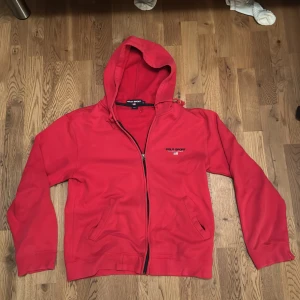 Röd zip-hoodie från Ralph Lauren - Säljer en snygg röd fleecejacka från Polo Sport Ralph Lauren. Den har en dragkedja framtill och en huva för extra mysfaktor. Perfekt för kyliga dagar och passar både till vardags och träning. Jackan är i bra skick och redo för nya äventyr! 🔥