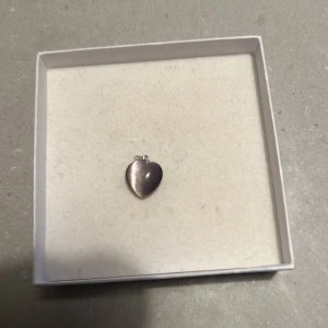 Hjärtaformad berlock i silver - Säljer en söt hjärtaformad berlock i silver. Perfekt att fästa på ett armband eller halsband för en personlig touch. Den har en slät och blank yta som ger en elegant look. Passar perfekt som en liten present eller för att komplettera din smyckessamling.