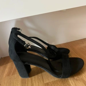 Svarta klackskor med remmar - Snygga svarta klackskor i mocka med remmar och spänne. Perfekta för festliga tillfällen. De har en bekväm klack och en stilren design som passar till många outfits.