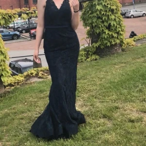 Mörkblå spetsklänning - Säljer en elegant mörkblå långklänning i spets. Klänningen har en vacker öppen rygg och smickrande passform. Perfekt för bal eller fest! Den har en v-ringad hals och knappar längs ryggen. Har använts 1-2 gånger. Priset kan diskuteras🩵