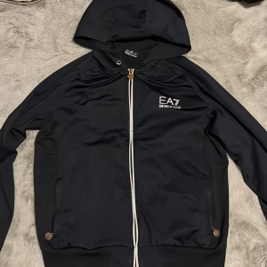Svart huvtröja från Emporio Armani - Säljer en snygg svart huvtröja från Emporio Armani EA7. Den är lite använd där av texten! Men i tyget o övrigt är den jättefin. Jag köpte den ny för ca 1100 o mitt pris e 600