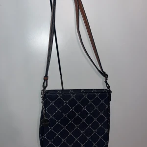 Marinblå axelväska från Tamais - Den har en dragkedja upptill och en praktisk ficka med dragkedja på baksidan. Insidan är fodrad med ett ljust tyg och har flera fack för enkel organisering. 