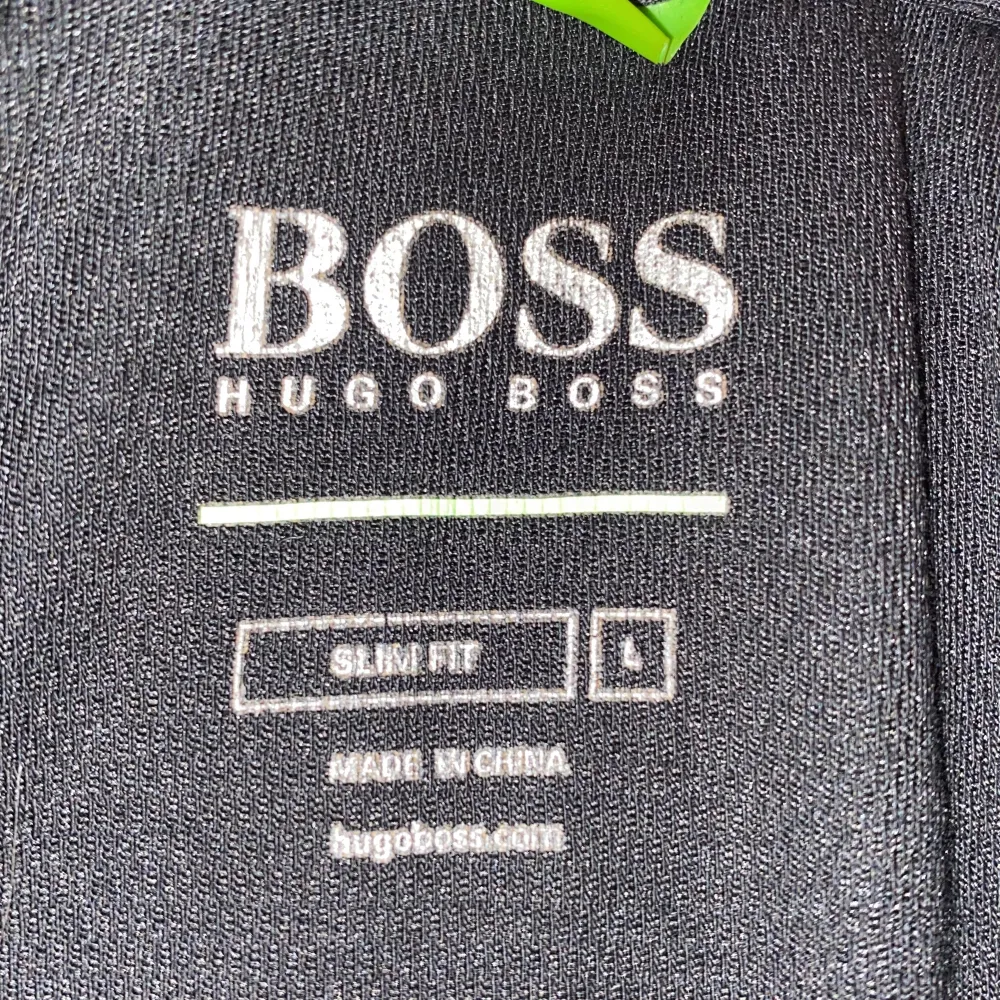 Snygg svart pikétröja från Hugo Boss i slim fit. Den har en klassisk krage med blå detaljer och knappar framtill. Perfekt för både vardag och fest. Tröjan har korta ärmar och är i mycket bra skick.. T-shirts.