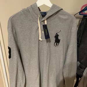 Ralph Lauren hoodie  - Ralph Lauren hoodie i grå färg. Storlek L. Nyskick med lappen kvar. Tveka inte på att skriva vid funderingar. Personen på bilden är 175cm. 