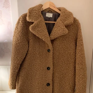 Beige teddyjacka från Nümph - Mysig brun teddyjacka från Nümph i mycket bra skick. Perfekt för höst och vinter! Jackan har långa ärmar och knappar framtill. Den är i en normal passform och har en klassisk krage. Perfekt för att hålla sig varm och stilren under kyliga dagar!